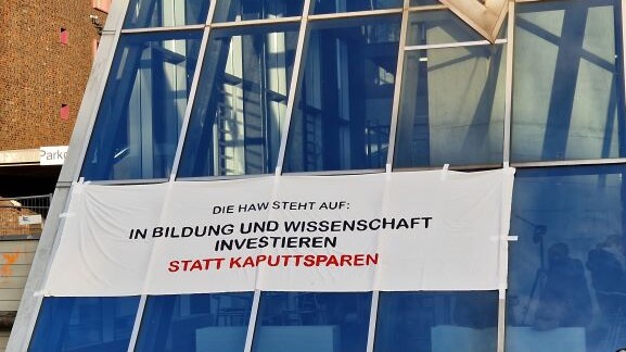 Das Foto zeigt ein Banner am Berliner Tor 5, auf dem steht: Die HAW steht auf: In Bildung und Wissenschaft investieren statt kaputtsparen.