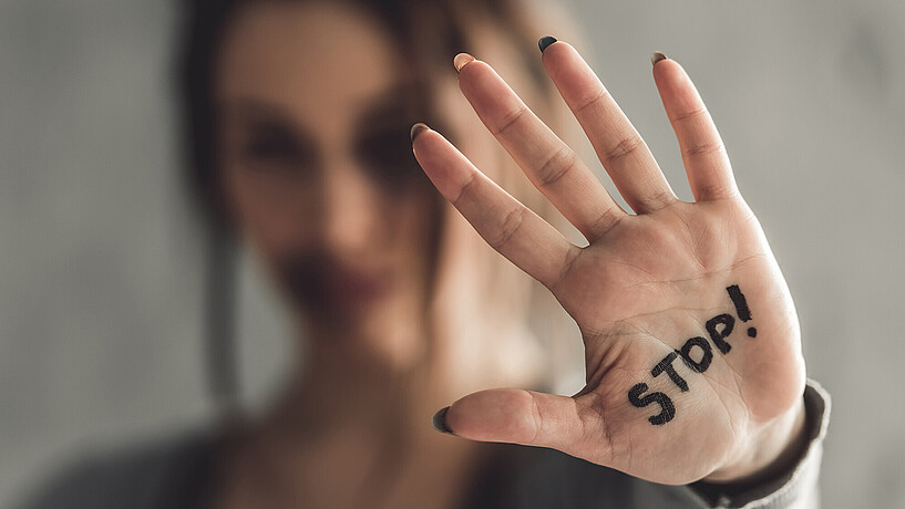 Eine Frau hält abwehrend ihre Hand hoch, auf der Stop geschrieben steht.