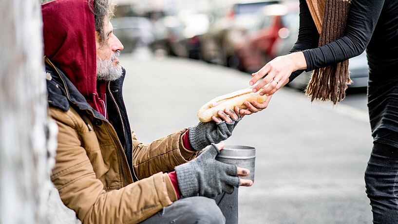 Eine Person überreicht einem Obdachlosen ein Stück Brot