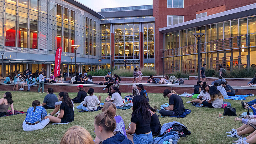 Eindruck vom Campus der NC State University Studierende sitzen auf einer Wiese vor einem Gebäude der NC State University