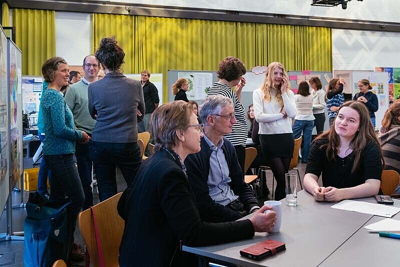 Einige Teilnehmende stehen an den Posterausstellungen hinter dem Arbeitstisch zum zkh-Projekt