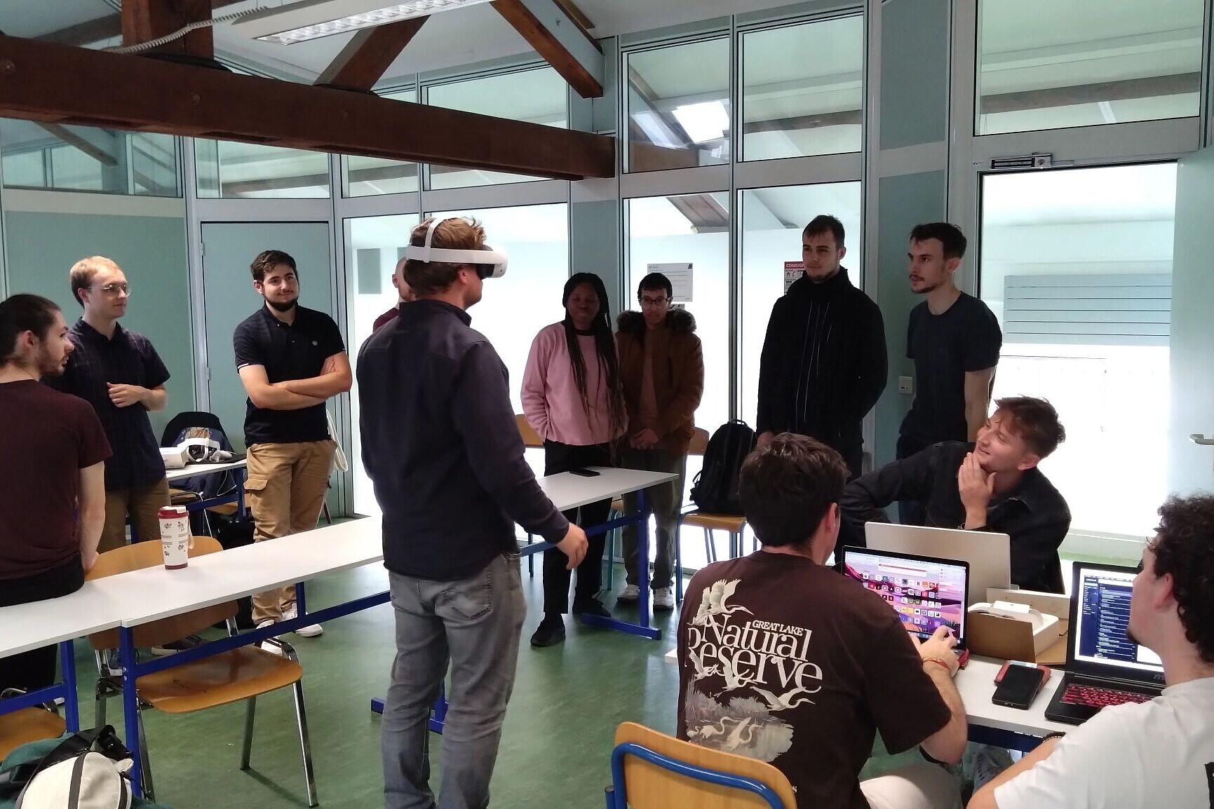 
                Meherere Personen stehen um einen Mann mit VR-Brille und beobachen ihn.
            