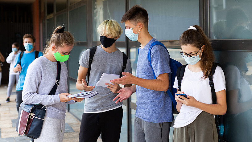 Junge Erwachsene mit Mundschutz und mobilen Endgeräten