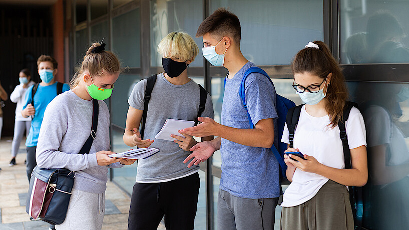 Junge Erwachsene mit Mundschutz und mobilen Endgeräten