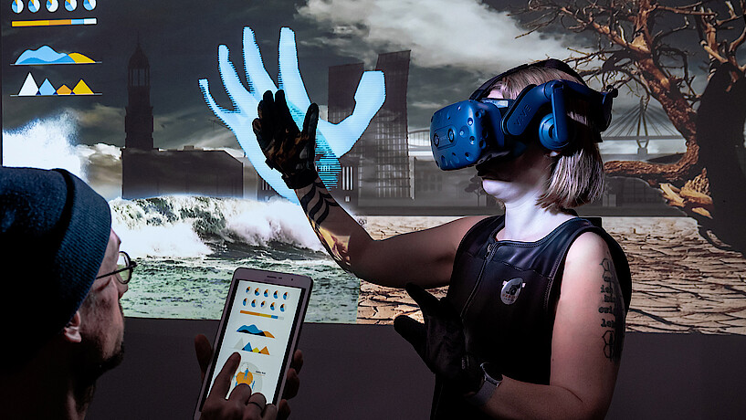 Frau mit VR-Brille und Handschuh vor einem Bildschirm