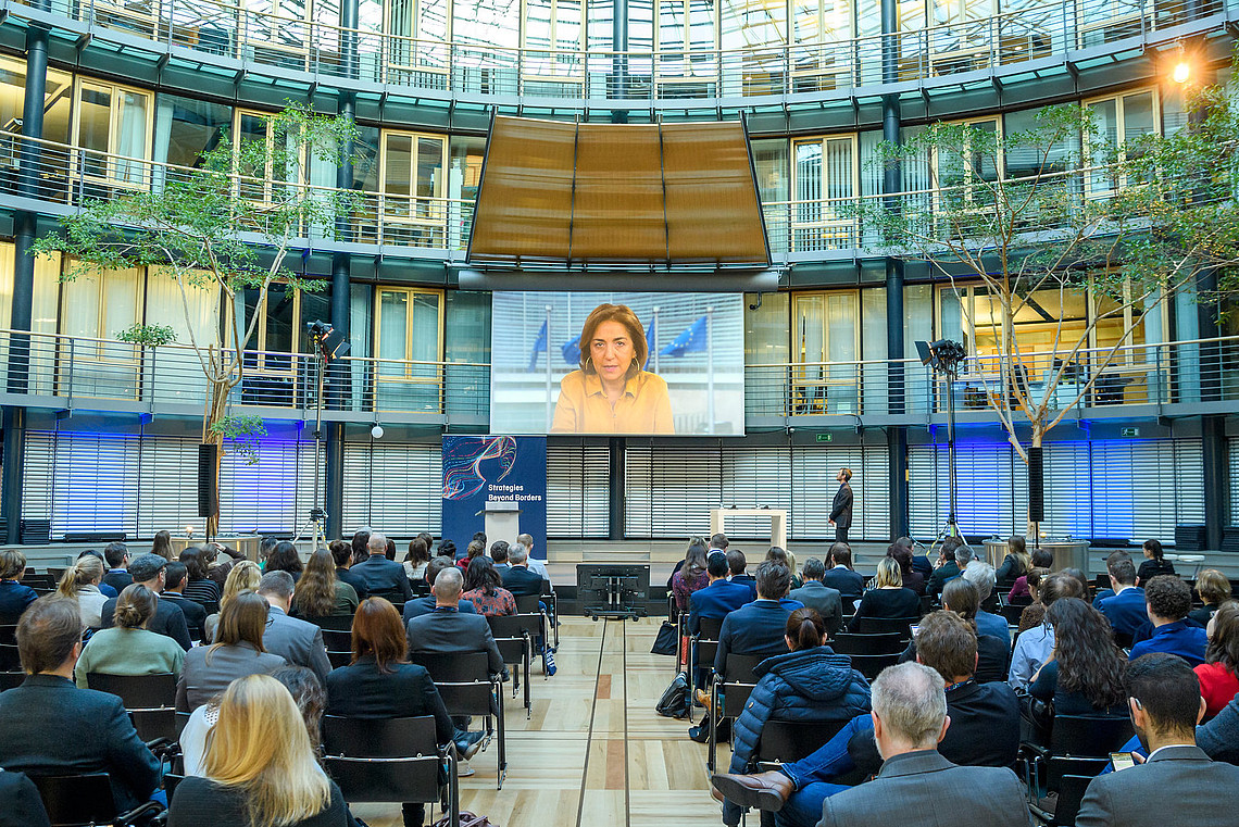 Das Bild zeigt das Plenum bei der HFD-Strategiekonferenz 2019 in Berlin. Das Publikum sitzt in einem Atrium. Auf der Bühne findet über eine Leinwand die Übertragung eines Grußwortes statt.