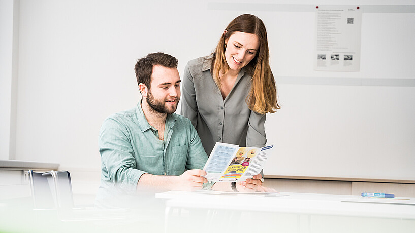 Zwei Personen (eine Frau und ein Mann) studieren ein Flyer des CareerService. (Symbolbild)