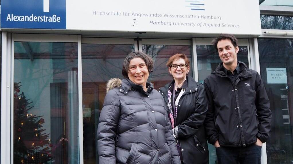 Three people standing in front of a university building 