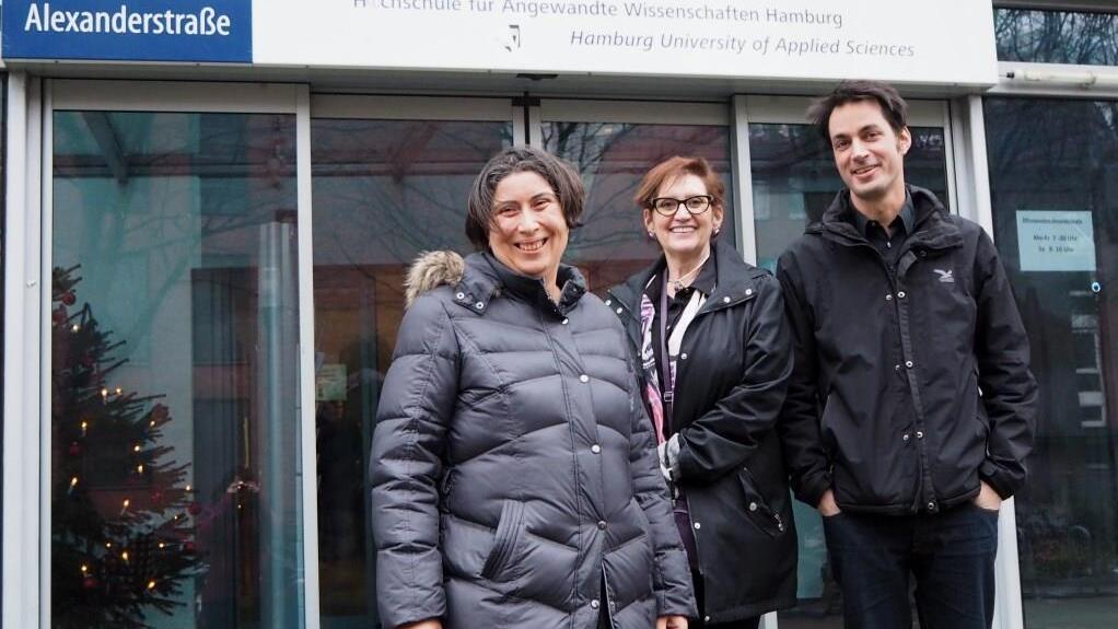 Three people standing in front of a university building 