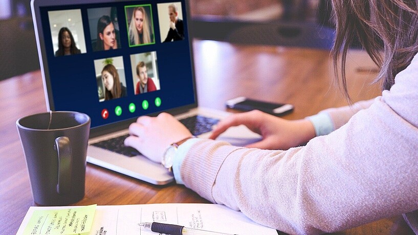 Frau sitzt am Schreibtisch vor aufgeklapptem Laptop mit Video-Konferenz