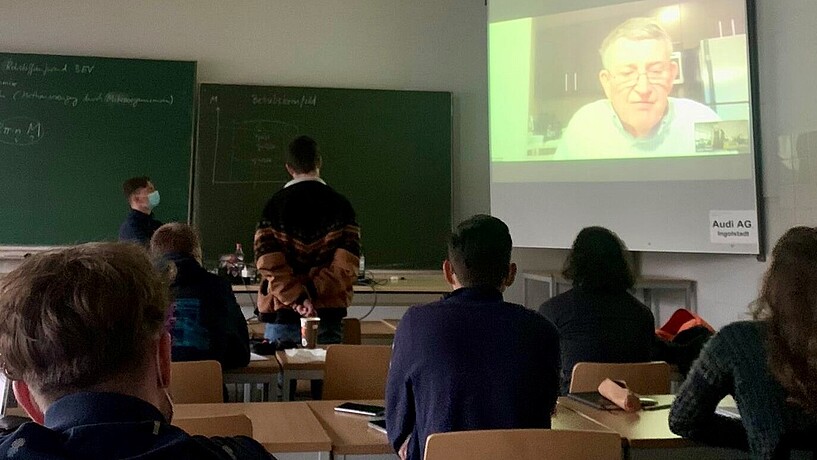 Seminarraum mit Leinwand und Studierenden, die einer Online-Vorlesung folgen