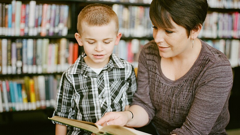 Eine Studierende schaut gemeinsam mit einem Grundschüler in ein Buch und erklärt etwas