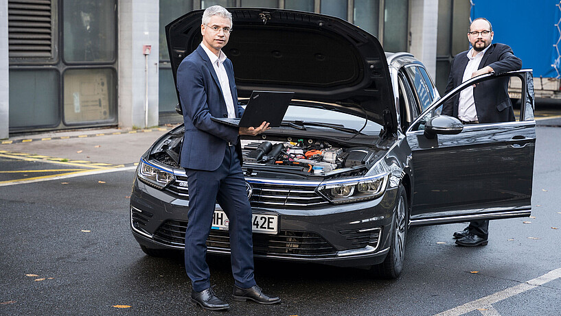 Prof. Hanno Ihme-Schramm (l.) und Prof. Thomas Netzel (r.) stehen vor einem Auto mit Hybridantrieb.