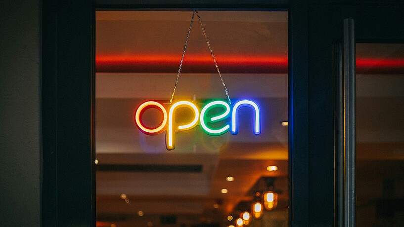Das Bild zeigt eine Leutereklame, auf der in bunten Buchstaben das Wort "open" steht.