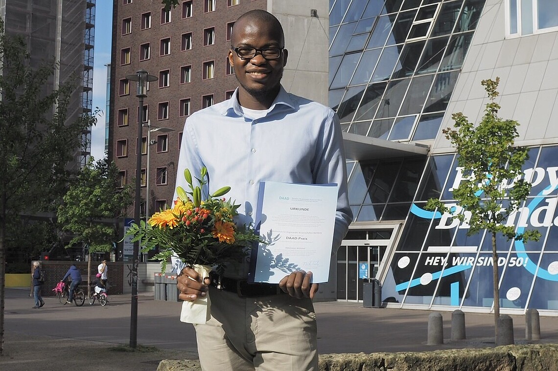 African student with prize certificate in front of university building