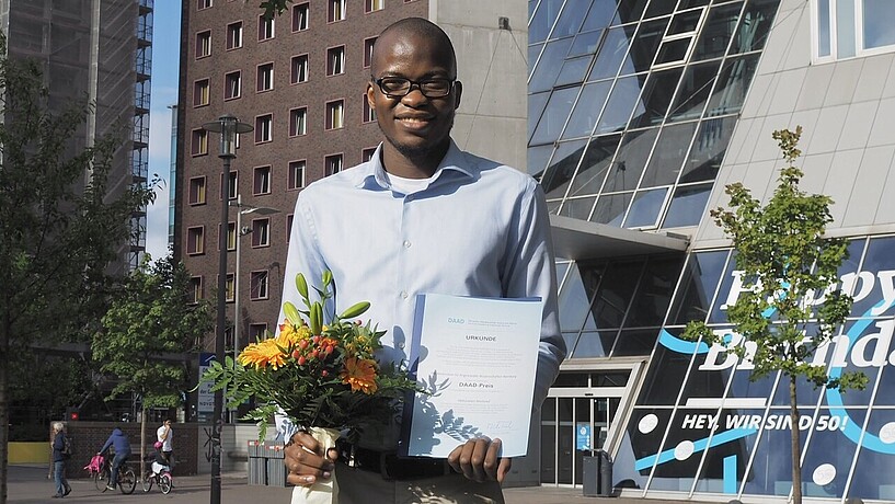 African student with prize certificate in front of university building