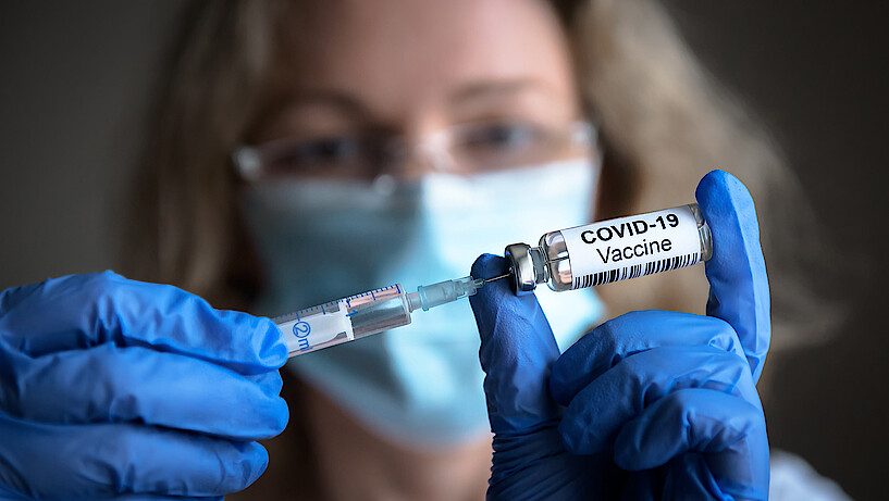Eine Frau zieht eine Spritze für eine Corona-Schutzimpfung auf.