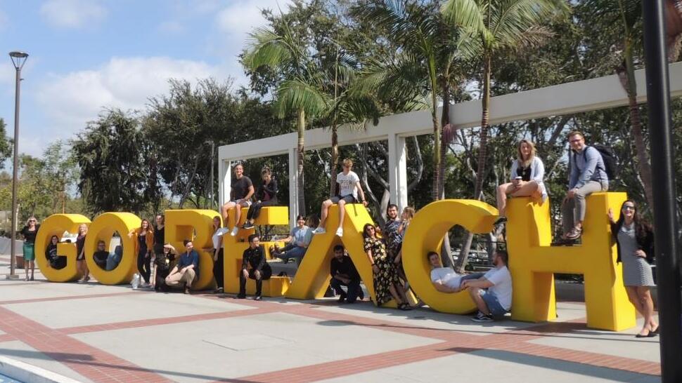 Group of students sitting on large letters that spell Go Beach