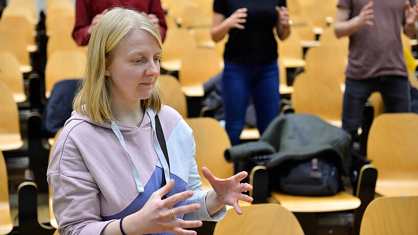 Studentin mit drei Studierenden im Hintergrund bei einem Workshop der Kompetenz-Werkstatt in einem Hörsaal.