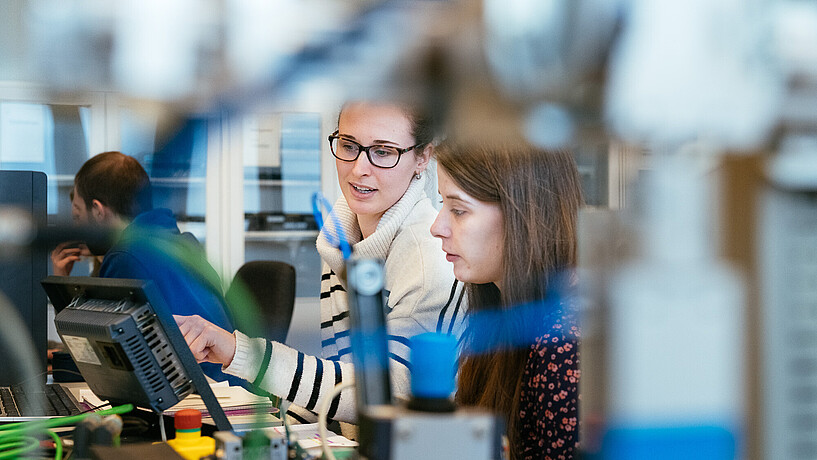 Foto zweier Studierenden. Im Vordergrund sind einige Kabel und Gerätschaften zu sehen.