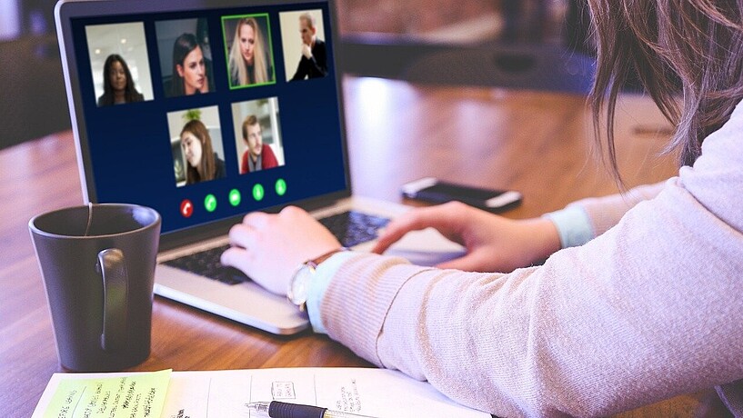 Person sitzt vor einem Laptop, auf dem Teilnehmende einer Video-Konferenz zu sehen sind