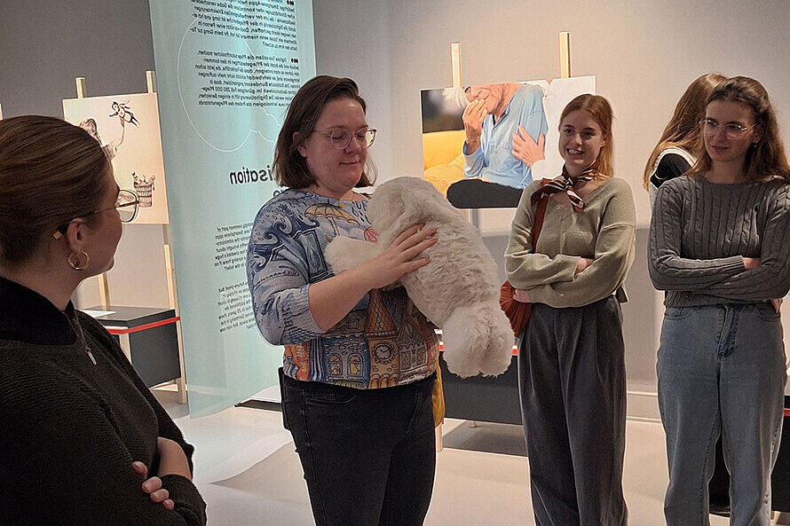 Die Teilnehmer:innen können in der Ausstellung den Pflegeroboter „Paro“ selbst testen. Die Therapierobbe „Paro“ wird z.B. in Altenpflegeheimen eingesetzt. Der Stofftierroboter reagiert auf Ansprache und streicheln. 