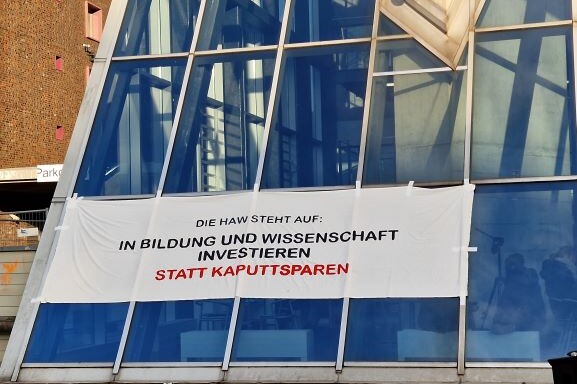 Das Foto zeigt ein Banner am Berliner Tor 5, auf dem steht: Die HAW steht auf: In Bildung und Wissenschaft investieren statt kaputtsparen.