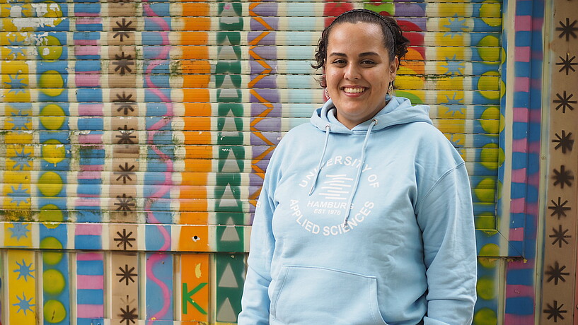 Female student smiling into the camera in front of a brightly painted container