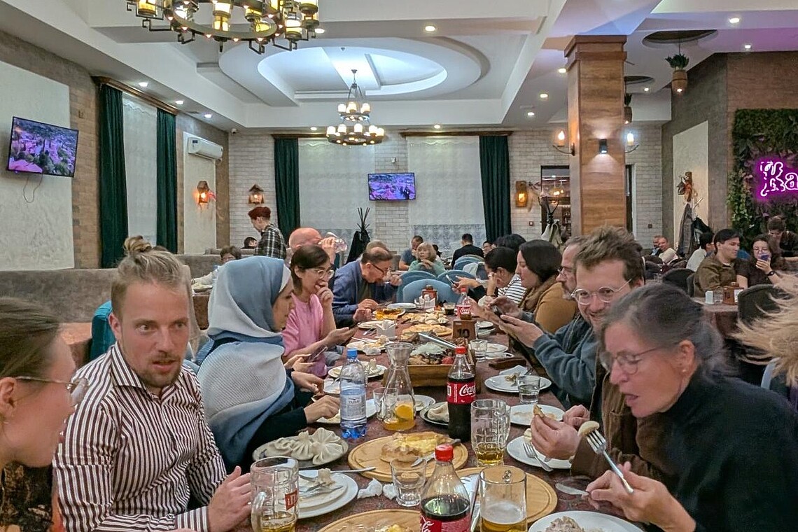 Viele Personen sitzen in einem Restaurant an einer langen Tafel und essen georgische Gerichte