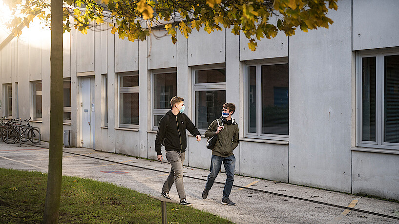 Zwei Studierende laufen nebeneinander auf dem Campus in Herbststimmung