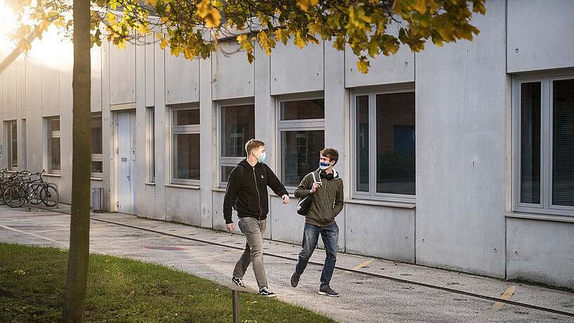 Zwei Studierende laufen nebeneinander auf dem Campus in Herbststimmung