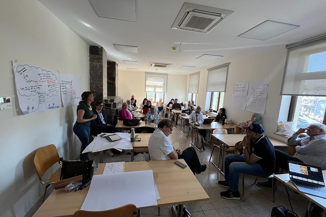 Seminarraum mit Studierenden und Professoer*innen, die sich angeregt austauschen