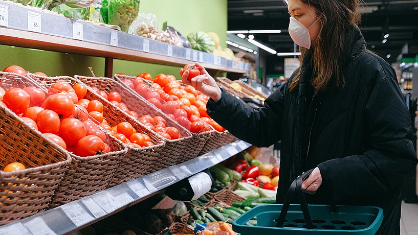 Eine Frau mit Gesichtsmaske vor einem Gemüseregal im Supermarkt