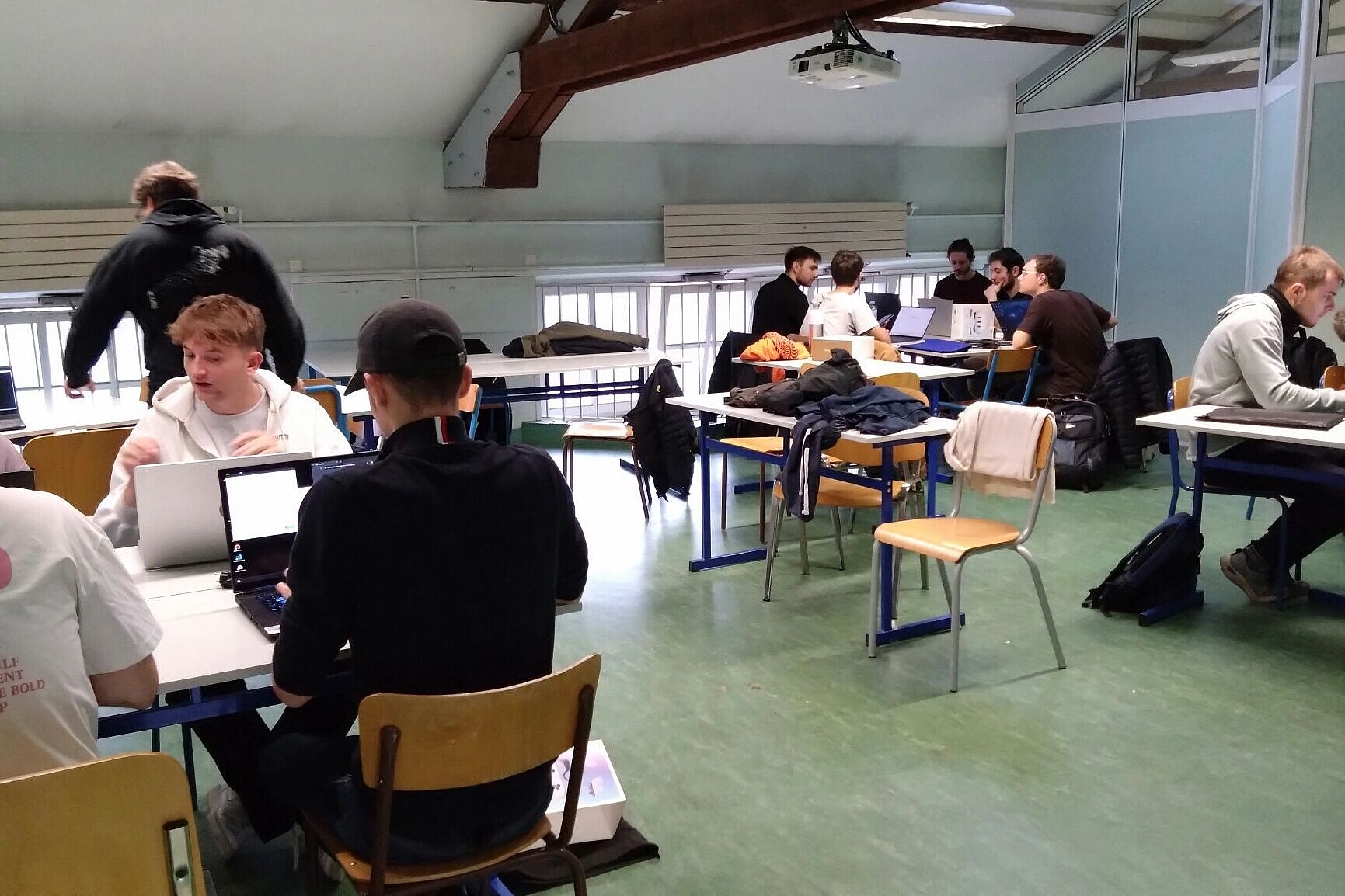 
                Etwa zwölf Teilnehmer:innen arbeiten an Tischen mit Ihren Laptops und diskutieren.
            