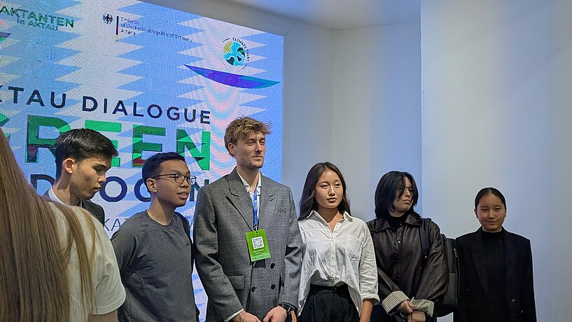 Studierende stehen auf einer Konferenz vor einer Leinwand mit dem Logo der Konferenz.