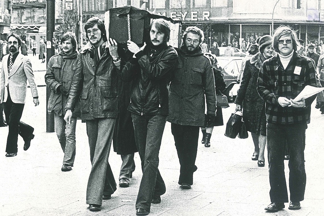 Schwarz-Weiß-Bild von protestierenden FH-Studenten 1977. Mehrere Studierende tragen symbolisch einen Sarg auf ihren Schultern.