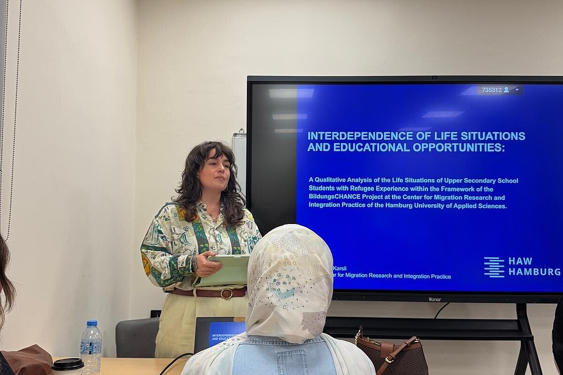 In einem Seminarraum steht eine junge Frau vor einem Screen und erzählt parallel zu einer Präsentation.