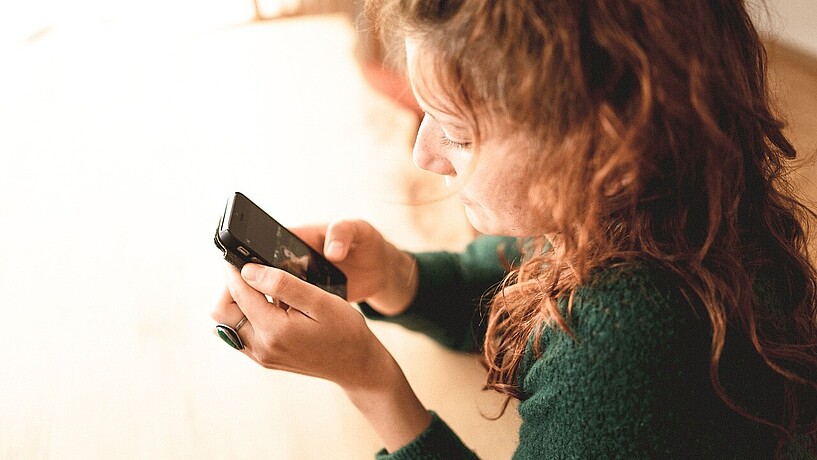 Frau sitzt am Tisch und schaut auf ihr Smartphone