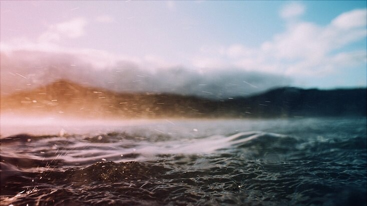 Das Foto zeigt eine Naturlandschaft mit aufgewühltem Wasser, Bergen und Wolken.