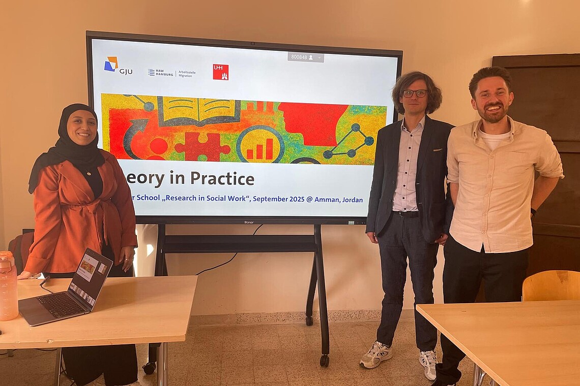 Vor einem Screen mit einer Präsentation stehen eine Studierende mit Hijab und zwei Professoren der Universität Hamburg.