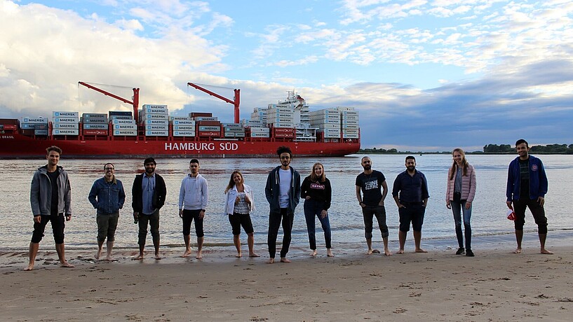 Studierende an der Elbe vor Containerschiff