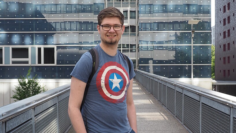 Male student standing in front of a modern glass university building