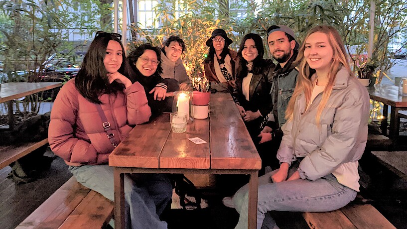 Sieben junge Studierende sitzen draußen an einem Tisch im Restaurant El Tigre in Hamburg und lächeln in die Kamera 