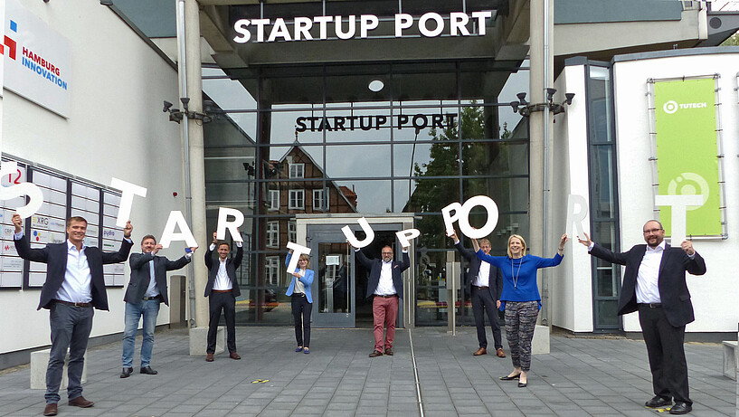 In der Harburger Schloßstraße 6-12 wurde über dem Gebäudeeingang der Schriftzug ‚Startup Port‘ enthüllt. Auf dem Foto zu sehen sind von links nach rechts:Tobias Redlich (HSU), Ralf Krappa (UKE), Jan-Paul Lüdtke (FH Wedel), Andrea Japsen (Leuphana), Martin Mahn (HI), Andreas Timm-Giel (TUHH), Jetta Frost (UHH), Thomas Netzel (HAW) 