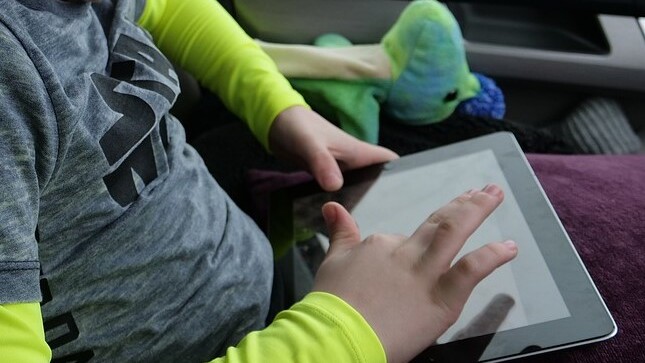 Das Bild zeigt ein Kind, das in einem Auto mit einem Tablet spielt.