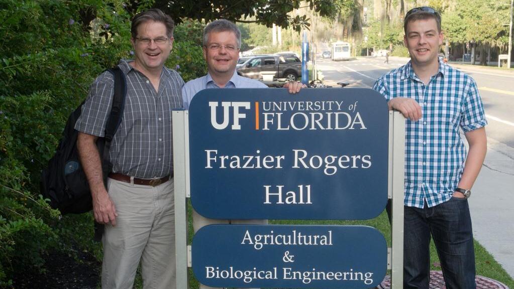 Three men standing in front of a university sign