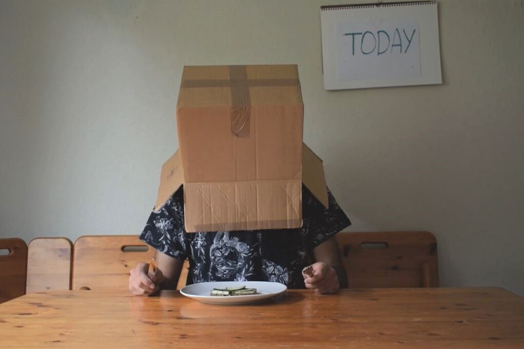 Person with cardboard box on his head sitting at a table