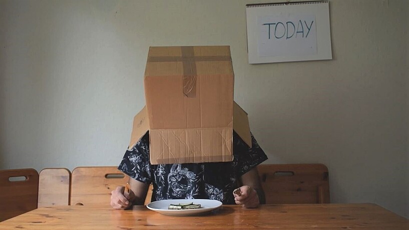 Person with cardboard box on his head sitting at a table