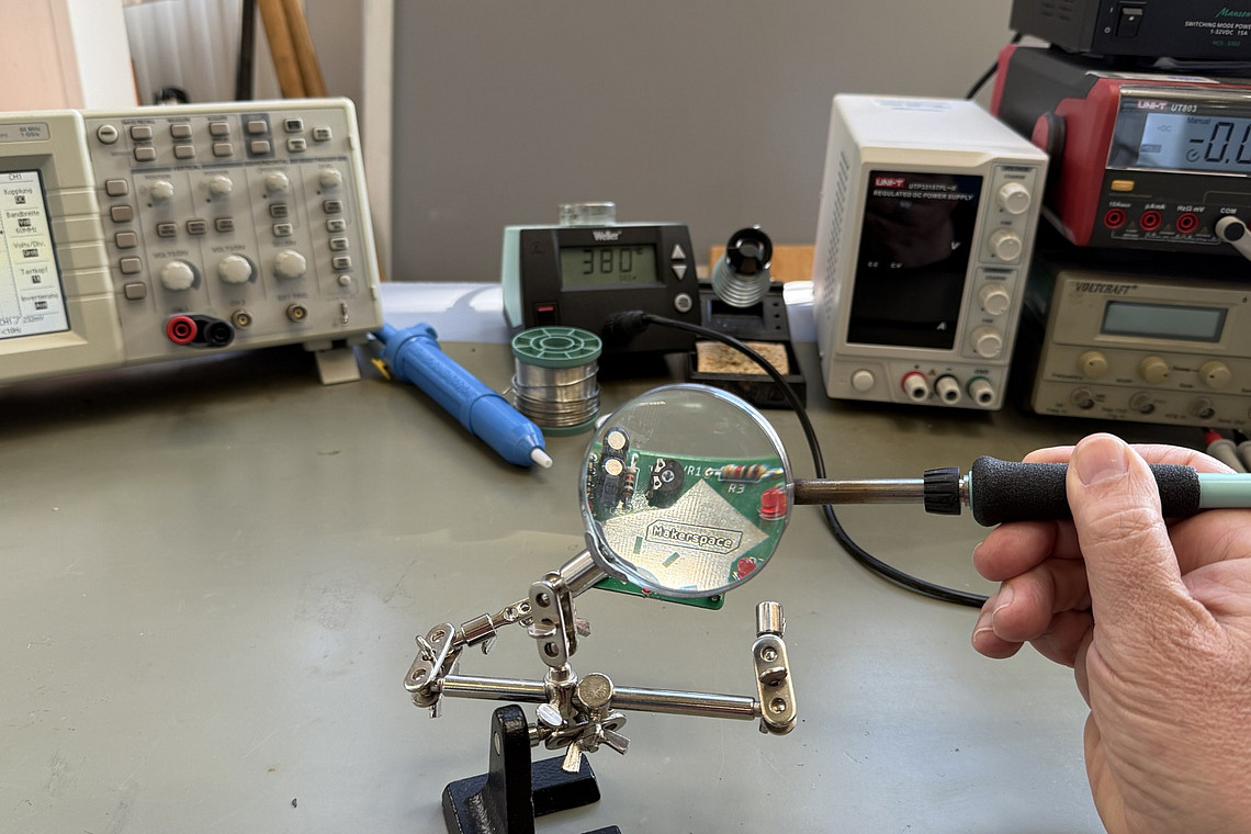 Eine Person lötet eine Platine. Auf der Platine steht "MakerSpace".