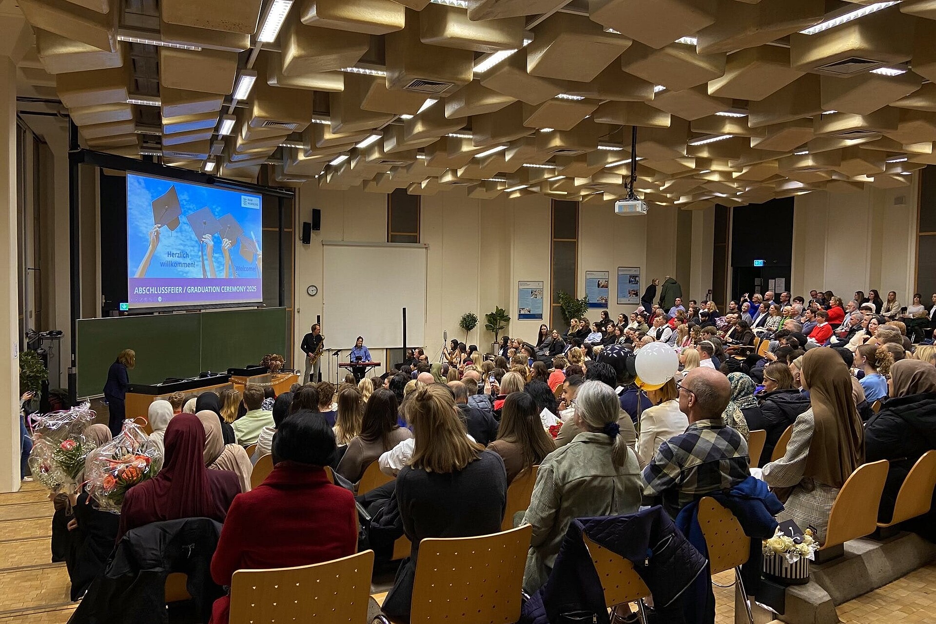 
                                                Im großen Hörsaal auf dem Campus Bergedorf warten die 70 Absolvent:innen und ihre Gäste auf den Beginn der feierlichen Zeremonie. 
                                            